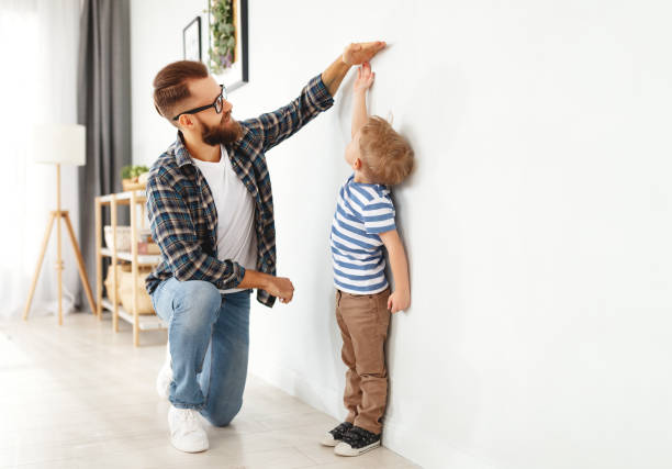 concept of development, growing up. a father measures height of his young child son