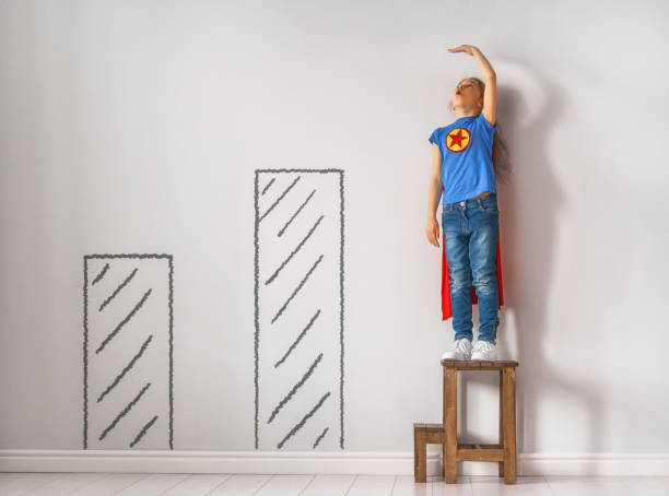 Little child is playing superhero. Kid is measuring the growth on the background of wall. Girl power concept.