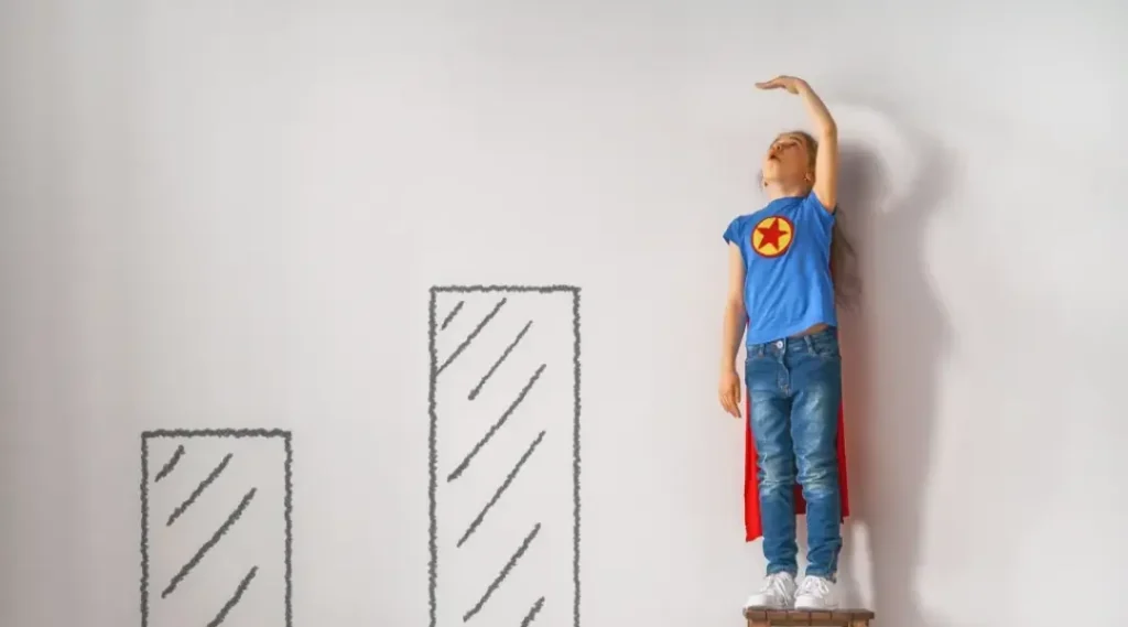 Little child is playing superhero. Kid is measuring the growth on the background of wall. Girl power concept.