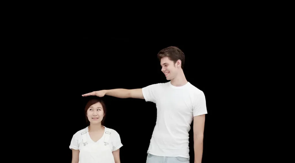 Tall man comparing height with a shorter woman against a black background